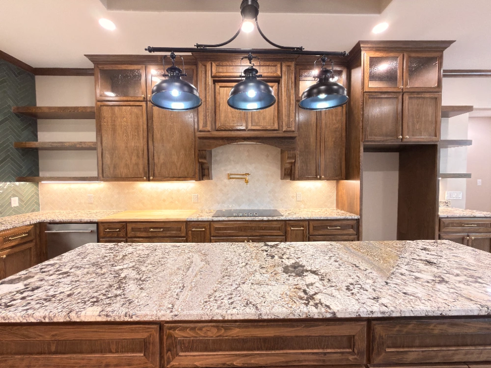 Custom stained wood kitchen cabinets with a granite island, black pendant lights and travertine backsplash in a Midland TX