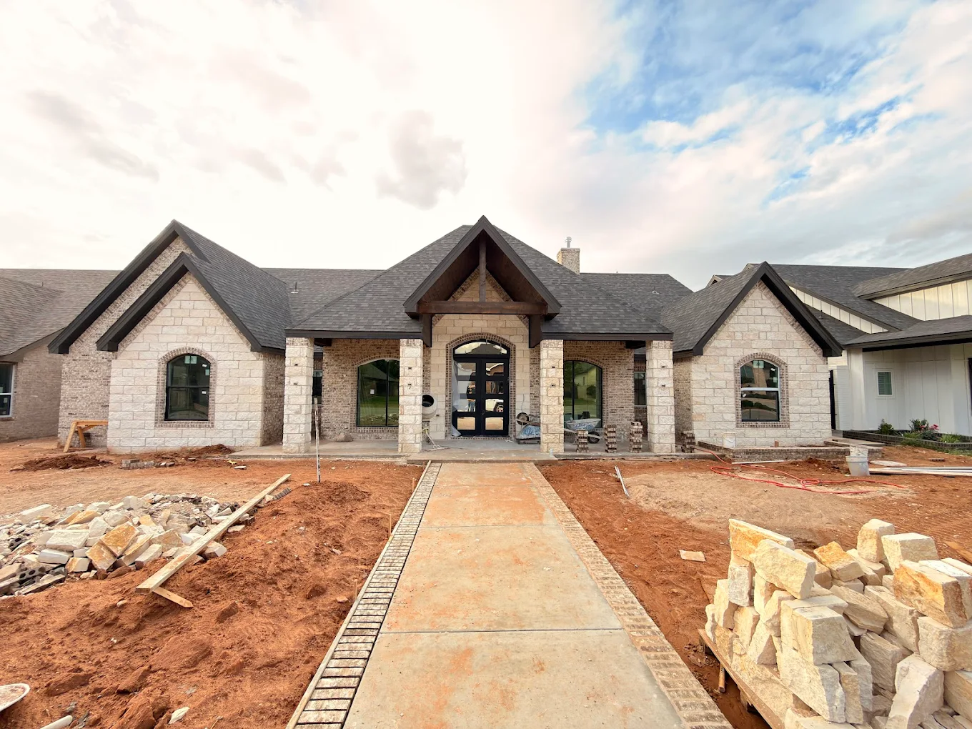 Custom stone and brick home under construction with stacked masonry and gabled roof in Midland TX