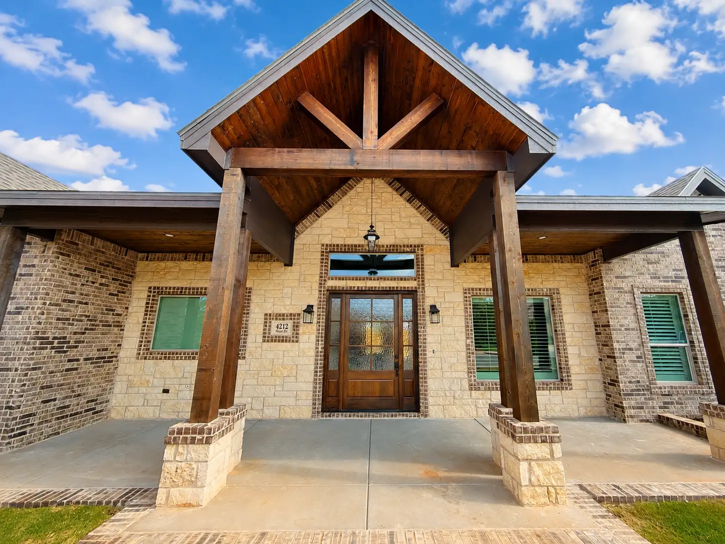 Luxury custom home exterior featuring wood beams, stone exterior, and covered porch in Midland, TX