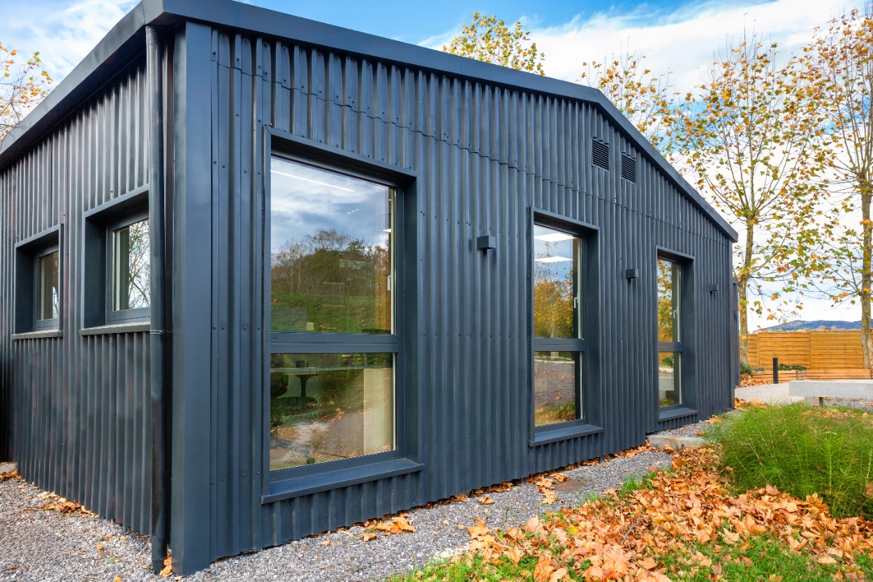 Small modern studio building clad in black corrugated metal with large windows