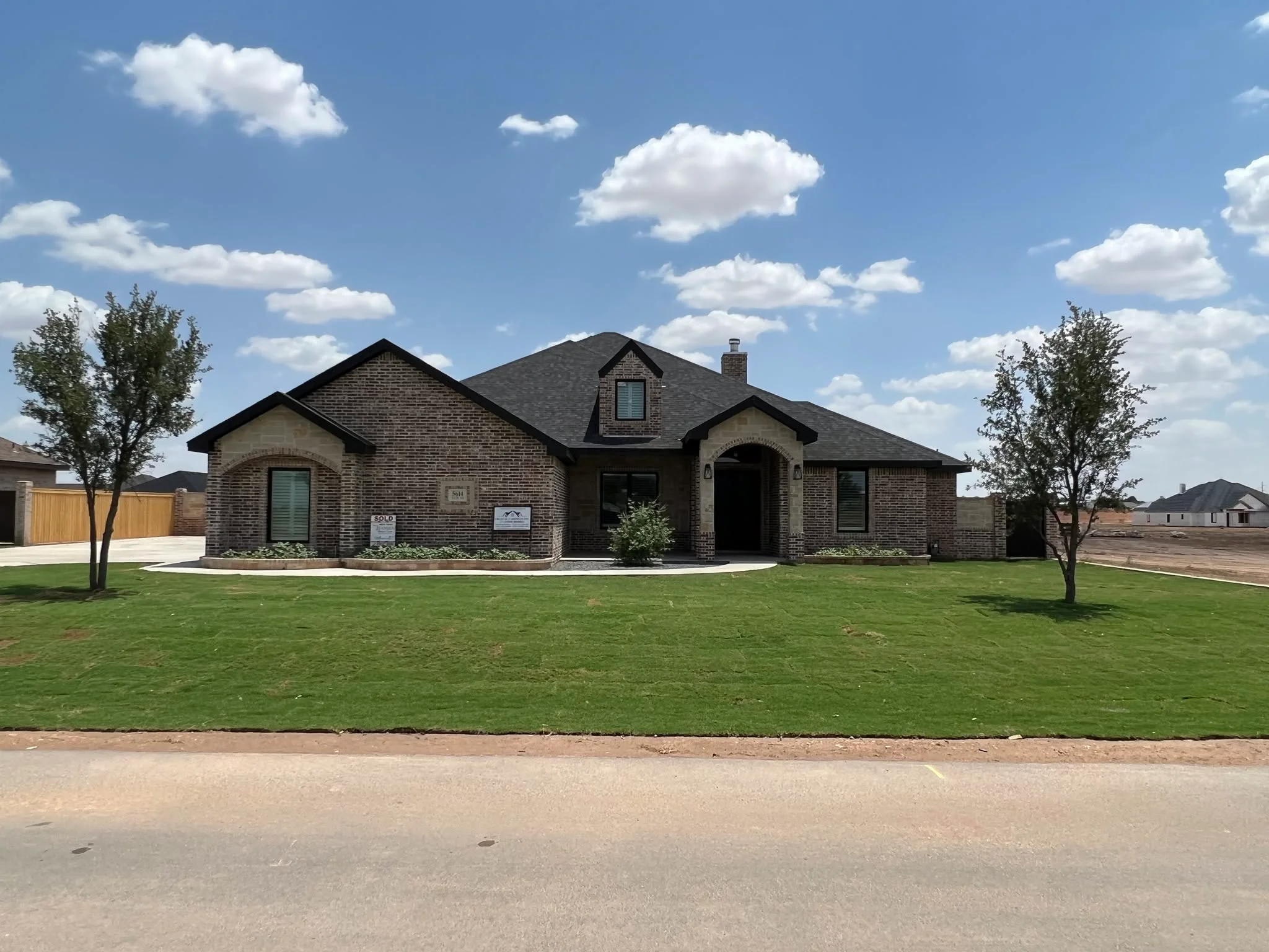 Custom dark brick home with stone accents, gabled roof and covered entry on a landscaped lot in Midland TX