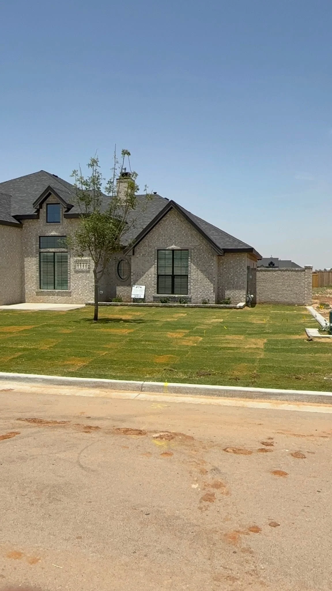 Custom grey brick home with black trim windows, gabled shingle roof and covered entry on a new lot in Midland TX