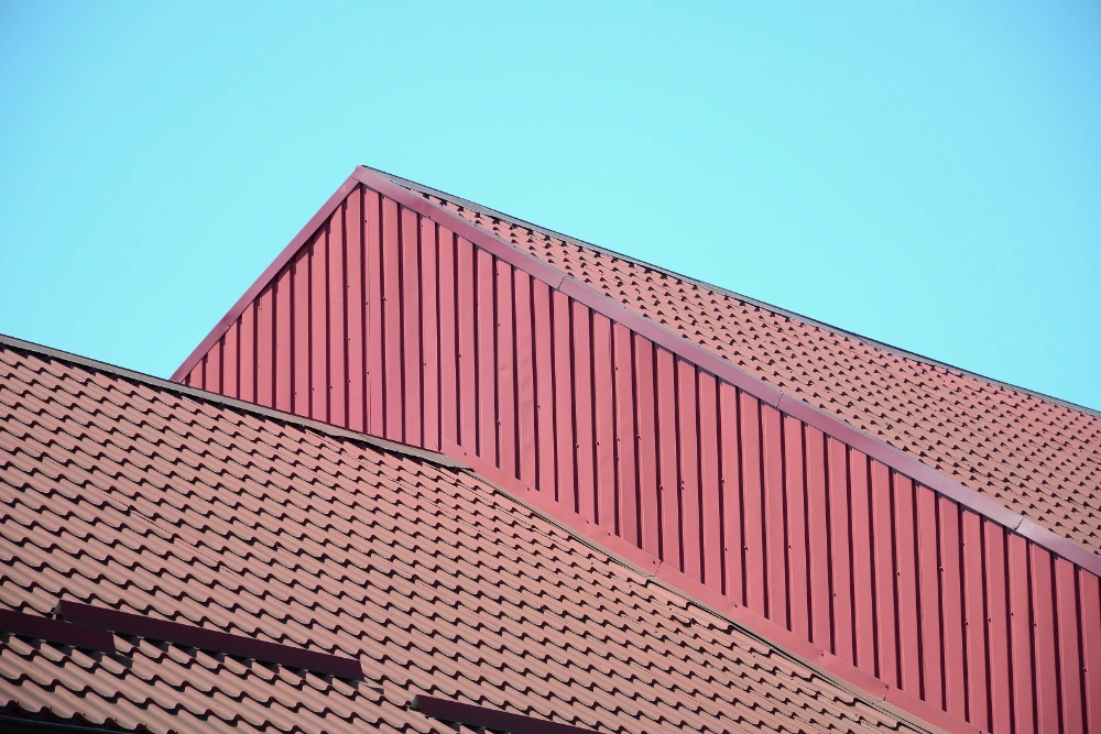 Red metal roof with standing seam panels and metal tile profile against a blue sky in Midland TX