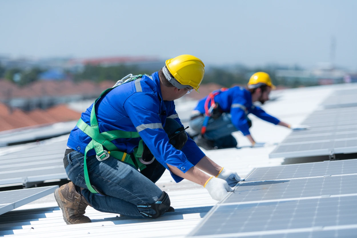 Technicians installing solar panels on a metal roof wearing safety harnesses in Midland TX