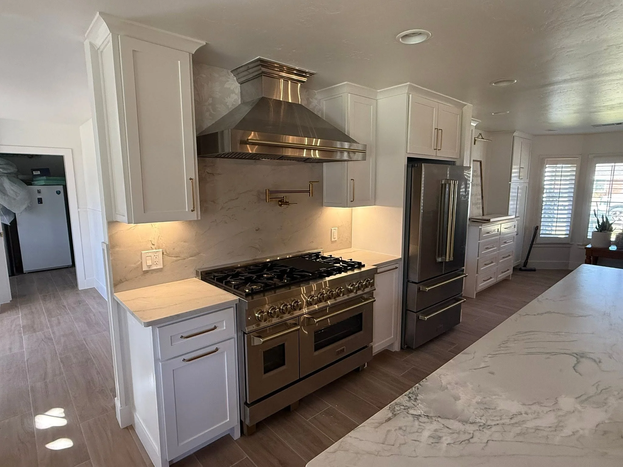 White kitchen cabinets with a stainless steel range, full height stone slab backsplash and white veined island in a Midland TX home