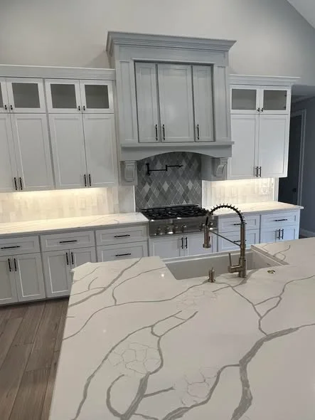 White quartzite kitchen countertops with soft grey veining, white cabinets and tile backsplash in a custom Midland TX home