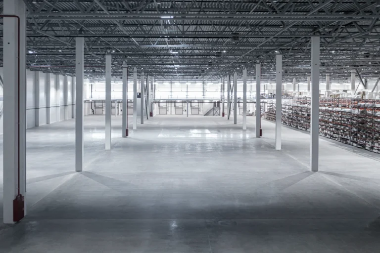 Spacious warehouse interior with steel support columns, open ceiling structure, and storage racking in the background in midland tx